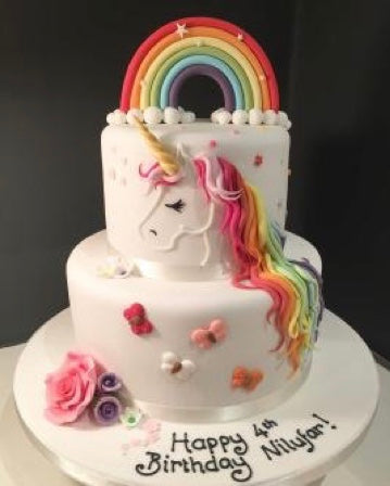white two tier birthday cake with rainbow unicorn on the side, a rainbow on top and sugar flowers and butterflies