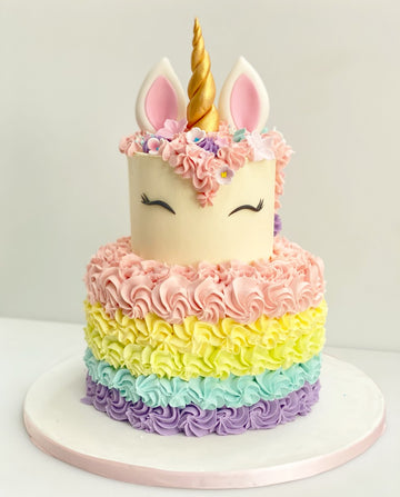 Buttercream two tier unicorn cake with unicorn head on top and buttercream rosettes on the bottom tier