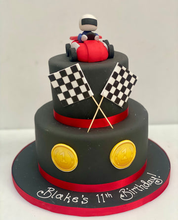 Two-tiered birthday cake with racing theme, including a go kart and checkered flags
