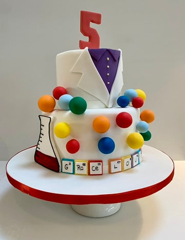 2 tiered birthday cake decorated like a chemist jacket and with chemistry themed decorations