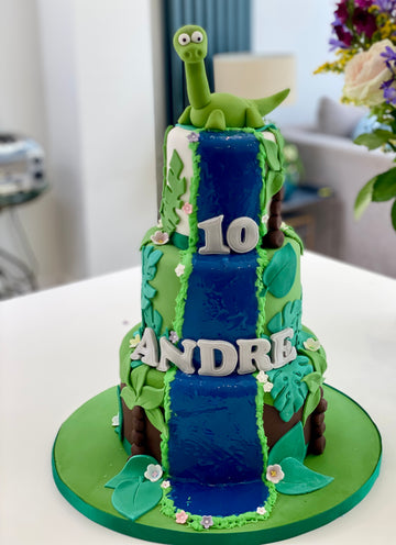 3 tier cake with waterfall down the front, dinosaur on top and tropical leaves