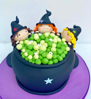 3 sugar Witches around a halloween themed cake decorated like a cauldron for Halloween party