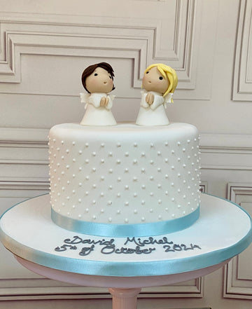 White cake with two angel figurines on top and polka dots around the sides