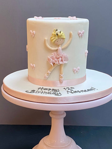Tall cake decorated with a ballet dancer on the front and lots of bows around to decorate