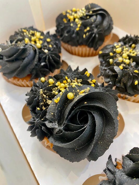 Cupcakes with black frosting and gold sprinkles on a white plate.