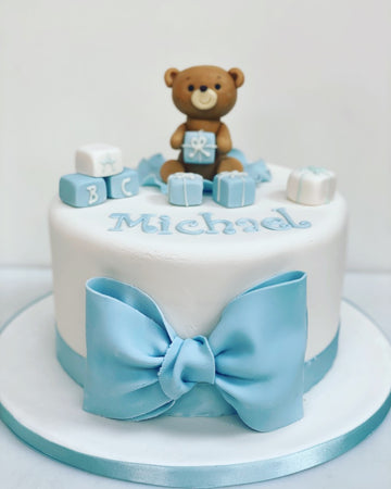 Christening cake with a teddy and toy blocks and a big blue bow on the front