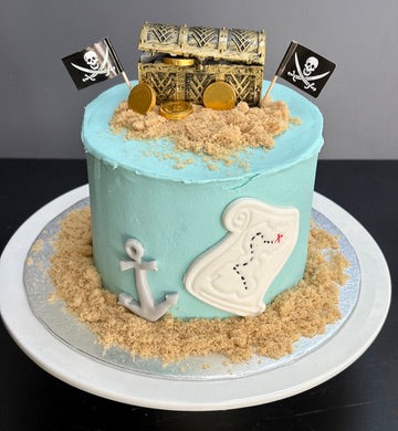 Pirate-themed cake with treasure chest, gold coins, and an anchor on a blue cake.