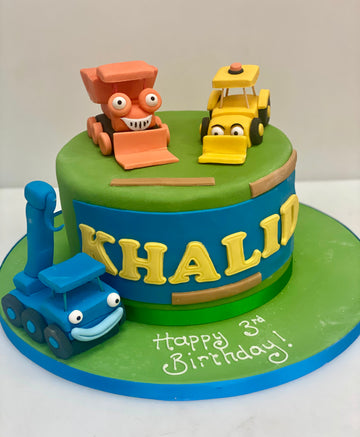 Birthday cake with toy truck and bulldozer decorations on a green and blue background.