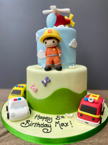 tw tier birthday cake with an ambulance, fire engine, police car and helicopter also an emergency services figure on it