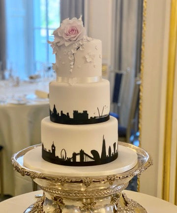 3 tiered wedding cake with city silhouettes around the sides including london and sugar flowers on top of the cake