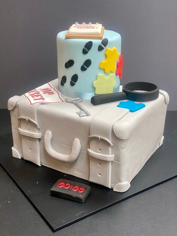 two tier birthday cake with elements of an escape room o decorate - the bottom tier is like a suitcase, there is a magnifying glass, puzzle, top secret sign