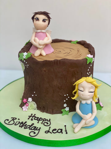Cake decorated to look like a tree log with fairies around it