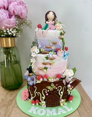 3 tier birthday cake decorated like a fairy house in a log, flowers, fairies and butterflies