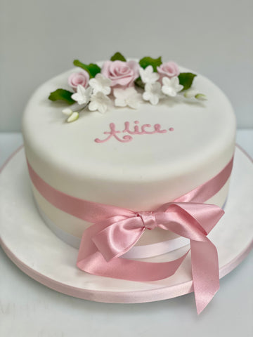White christening cake with pink ribbon and floral decorations on a white background