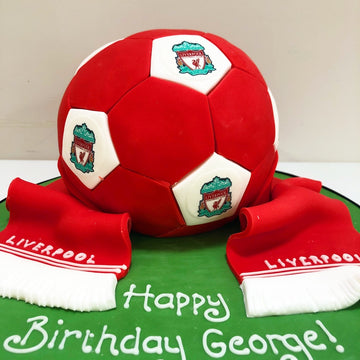Red and white soccer ball cake with Liverpool FC logo and scarves on a green base