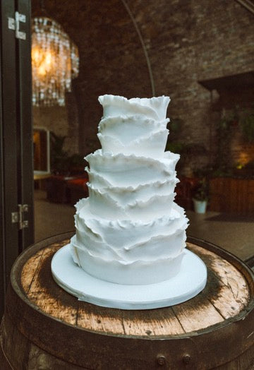 White ruffled wedding cake on 3 tiers, on a wooden barrel with a rustic background