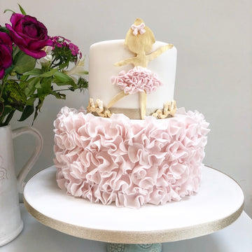 Two-tiered cake with pink ruffled bottom tier and white top tier with ballerina figurines,