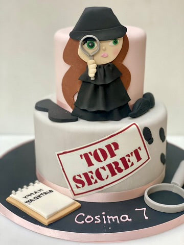 Spy themed birthday Cake decorated with a figure holding a magnifying glass, wearing a detective outfit, and featuring a 'Top Secret' stamp.