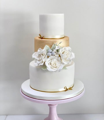 Gold and White 3 Tier Wedding Cake with white bouquet of sugar flowers in the middle of the design