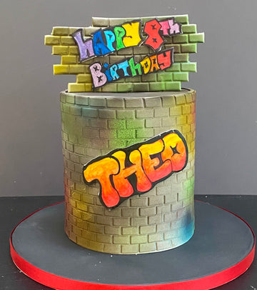 Birthday cake decorated wtih graffiti and a brick wall motif