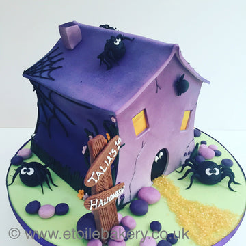 Halloween-themed cake designed like a haunted house with spiders and cobwebs.