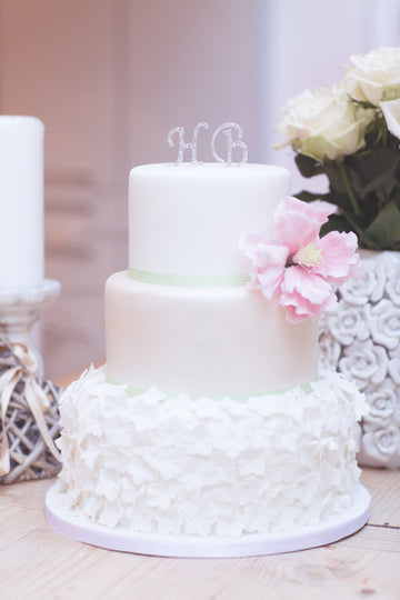 3 tiered wedding cake with hydrangea flowers all over the bottom tier and a pink sugar peonie