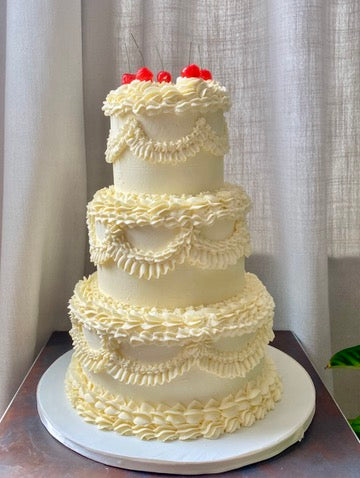 Three-tiered lambeth piping white wedding cake with ruffled design and red cherries on top
