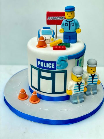Birthday cake decorated in the theme of lego city with police lego figures by a cake that looks like a lego police station