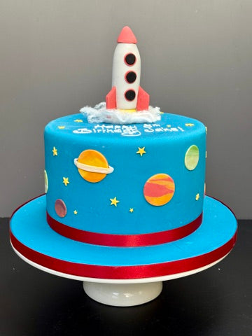 blue birthday cake with a rocket on top and planets and stars to decorate