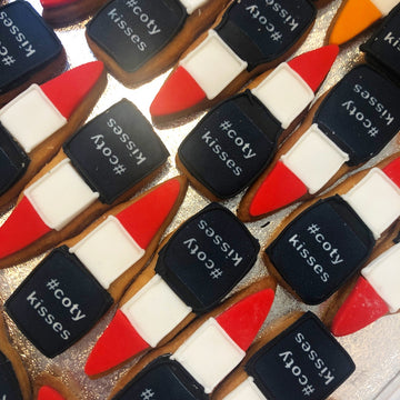 Branded Cookies shaped like lipsticks with 'coty kisses' text on a glittery surface