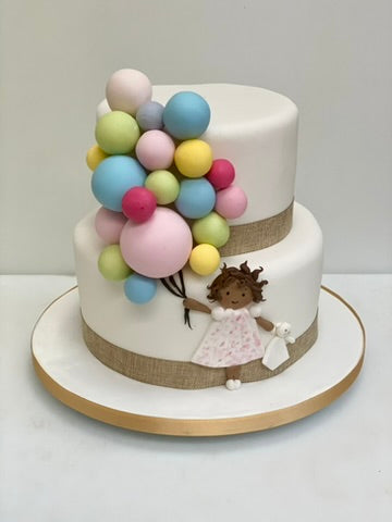 Two-tier cake with colorful balloons and a figurine of a girl on a white background