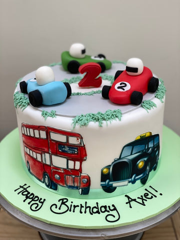 Birthday cake with toy cars and a double-decker bus and london taxi on a white background