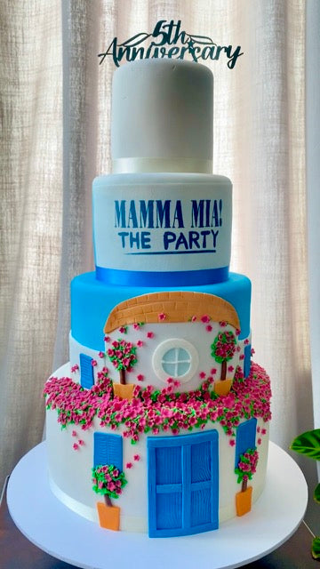 Mamma Mia Themed Cake on 3 tiers with the House from Mamma Mia on the front and the party logo