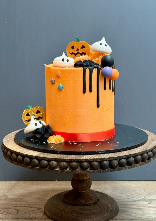 Halloween themed cake with meringue ghost decorations, a black drip, sparkly pumpkins and halloween balls