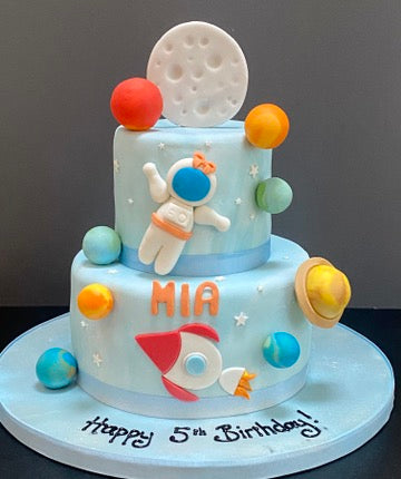 Two-tier pale blue birthday cake with space theme, including an astronaut figure and planets