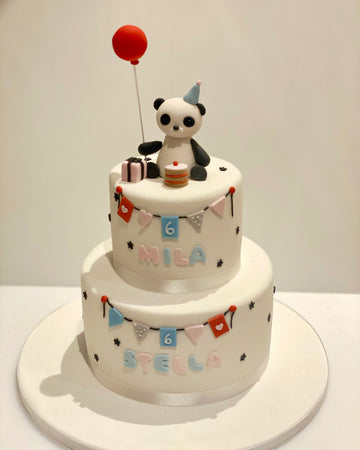 Birthday cake with a panda and balloon topper and bunting around the sides