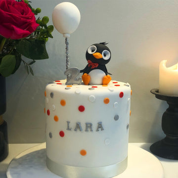 Birthday cake with a penguin and a balloon on top