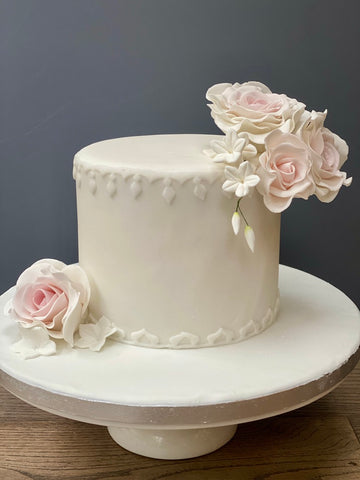 Small white wedding cake with sugar pink roses and piped detailing around the edges