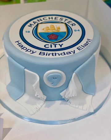 Round cake with Manchester City logo and scarf around the sides