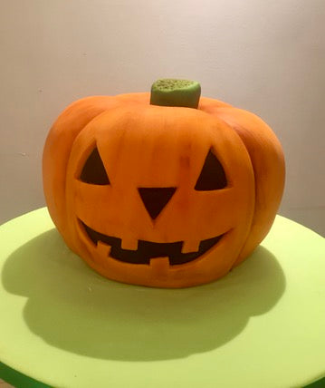 Jack-o'-lantern pumpkin halloween cake on a green cake stand with a plain background