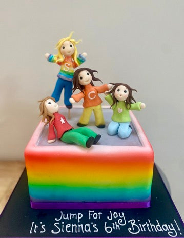 Birthday cake decorated to look like a rainbow trampoline with sugar figures jumping on top