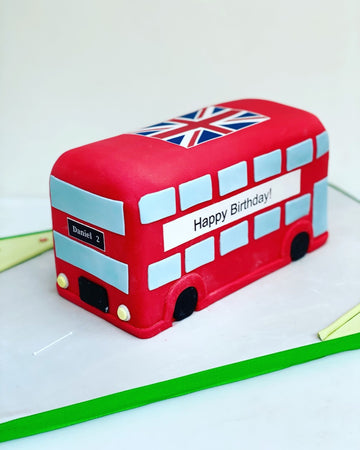 Red double-decker bus-shaped birthday cake with a Union Jack flag on a white background
