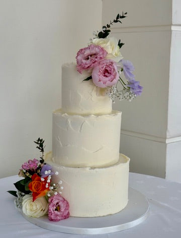 Rustic textured buttercream wedding cake on 3 tiers finished with fresh flowers like peonies and roses