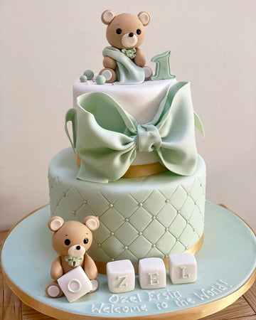 Sage coloured cake decorated with two teddy bears, a big bow, quilted effect and blocks