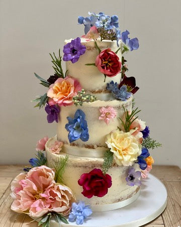 a 3 tiered semi naked wedding cake decorated with colourful silk flowers