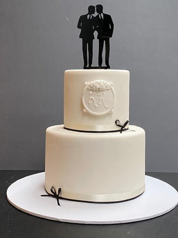 Simple minimalist white gay wedding cake with topper of 2 men, plaque with initials and thin black ribbon and bows