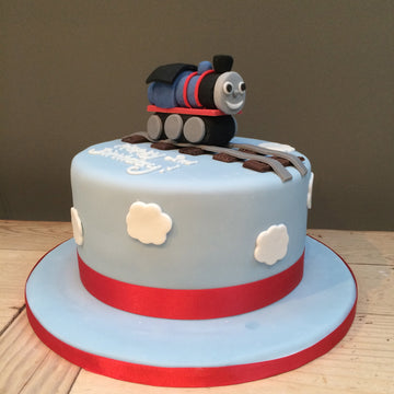 Thomas the tank engine figure on top of a blue cake with clouds