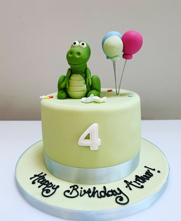 Birthday cake with dinosaur on next to bunch of balloons