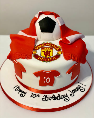 Birthday cake with Manchester United theme, including a soccer ball, scarf, and jersey.