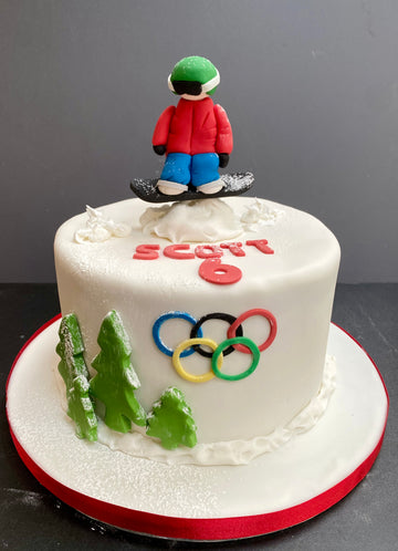 White cake with Olympic rings and a snowboarder figurine on top